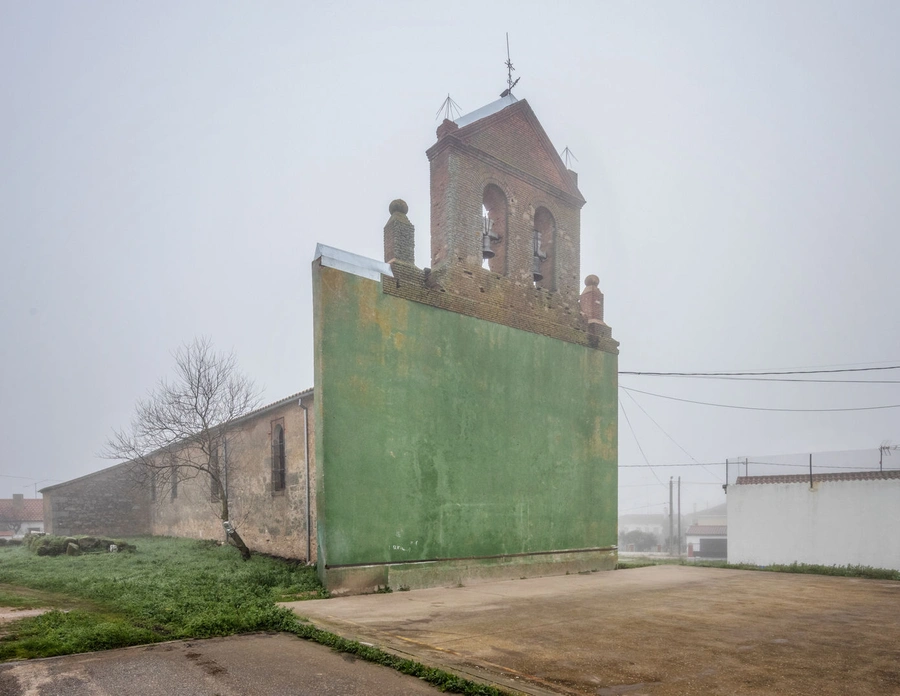 Brick bell tower rising above a tall green wall in a foggy, rural scene