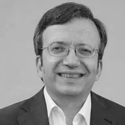 Head-and-shoulders portrait of a smiling man wearing glasses and a dark suit with a white shirt.