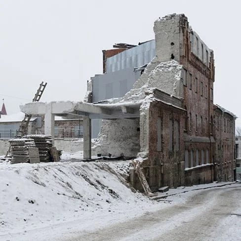 Ruined brick building covered in snow with crumbling walls and exposed concrete framework on a wintry street.