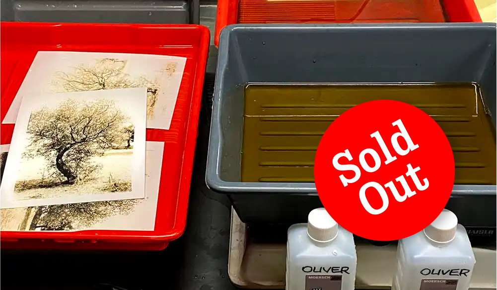 LithDevTrayDeveloper-Sold out Red bin with tree-print artworks beside a gray tub filled with brown liquid; a large red 'Sold Out' sticker overlaps the tub; two white bottles labeled Oliver in front.