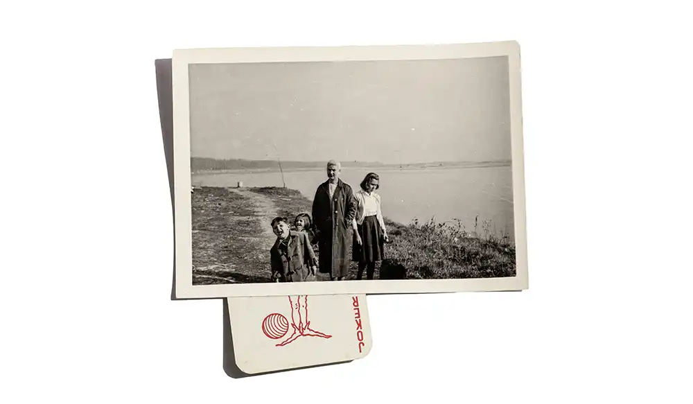 _MG_0598 copia Black-and-white photo of a family of four—two adults and two children—standing on a coastal path by the water, with a stack of photos beneath it.