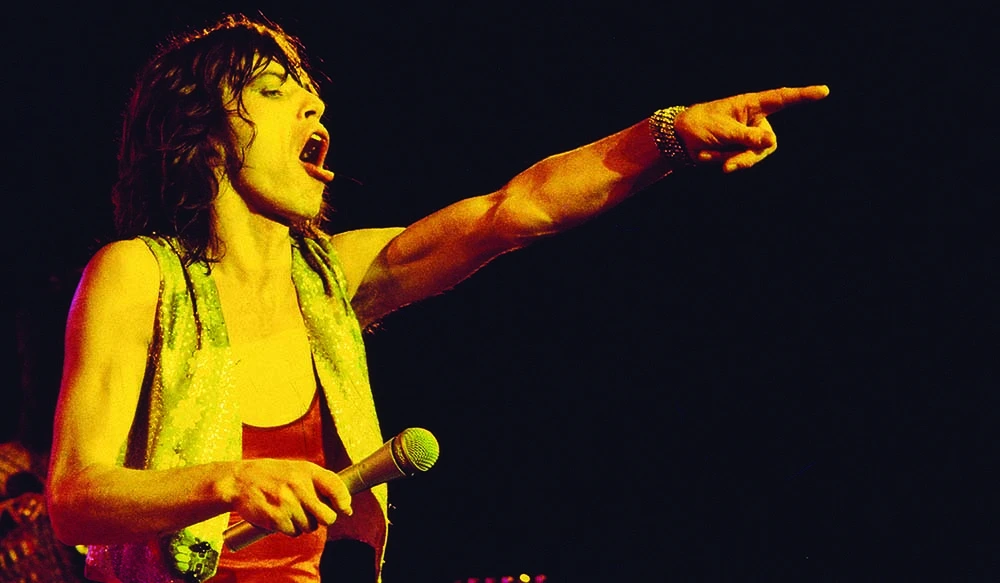 Male rock singer on stage, microphone in hand, shouting and pointing into the crowd.