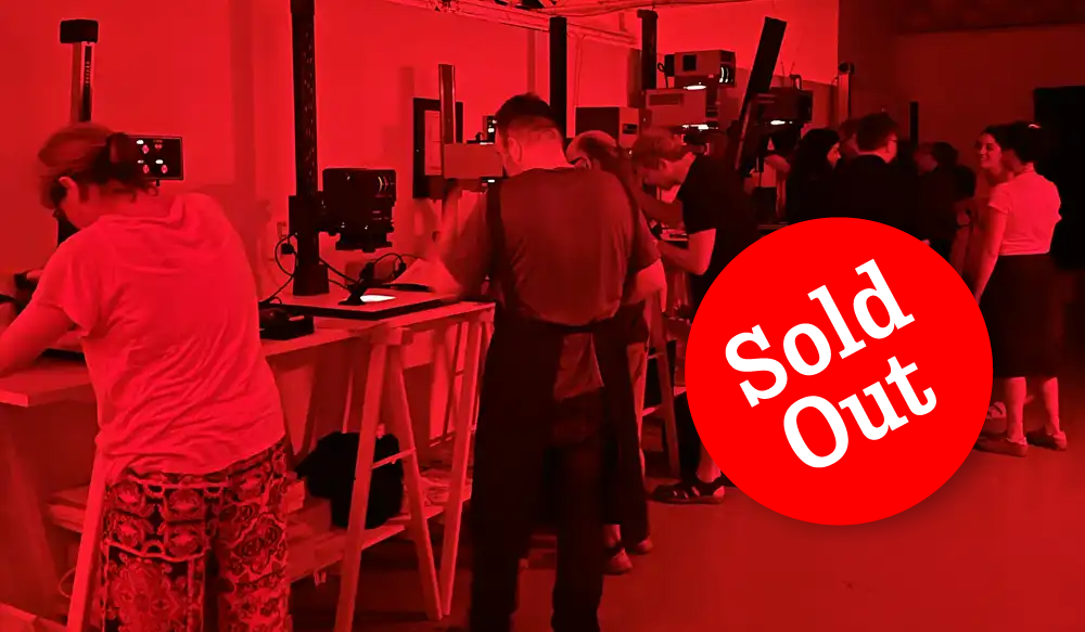 Laboratorio-Revelat-sold out - Revela't 2026 Crowd of attendees at a workshop or tech lab, standing at benches with equipment; red tint and a large 'Sold Out' badge overlaying the scene.