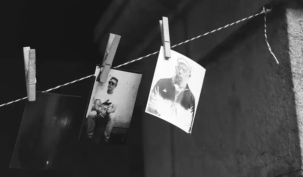 chechu-taller-1000x583px - Revela't 2026 Black-and-white photos clipped to a clothesline with wooden clothespins, hanging against a dark textured wall.