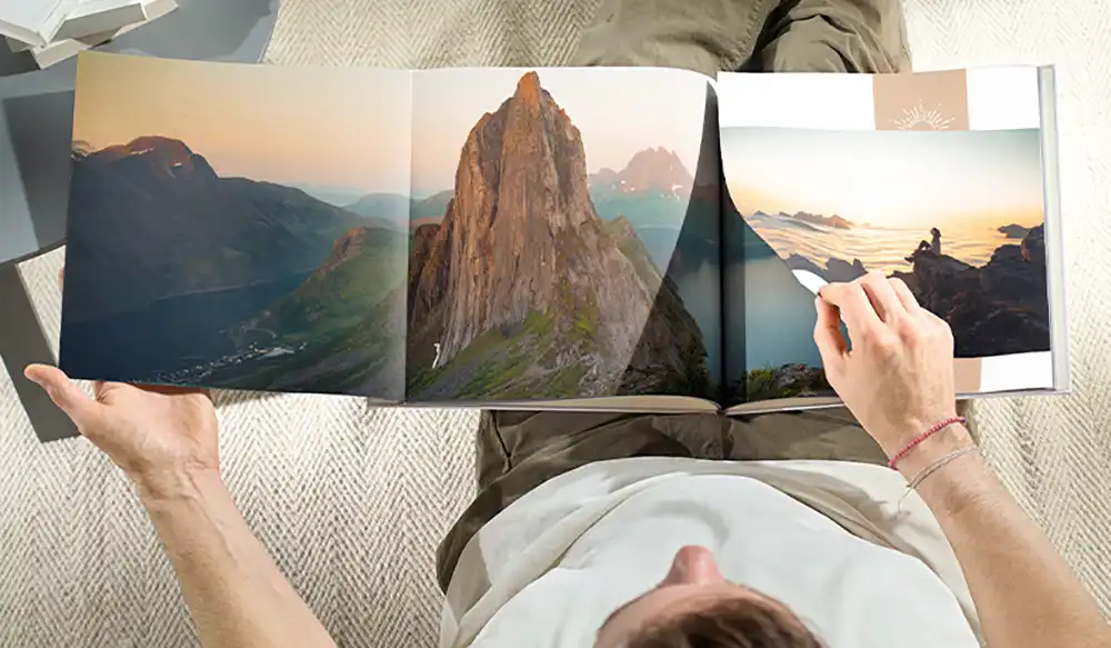 Cewe taller - Revela't 2026 Top-down view of a person holding an open photo book showing a rugged mountain landscape across two pages.